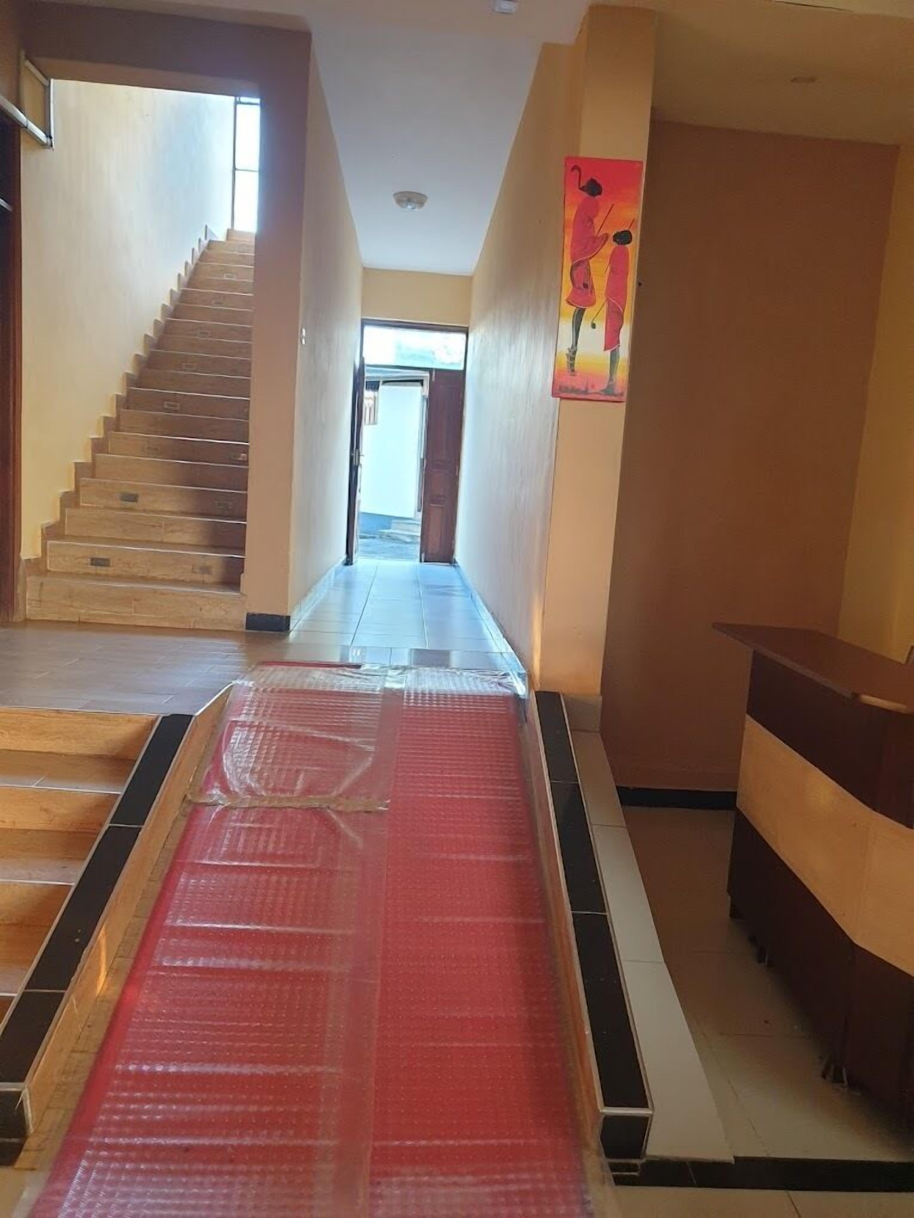 A hallway with a staircase on the left, a red carpeted area in the center, and a reception desk on the right.