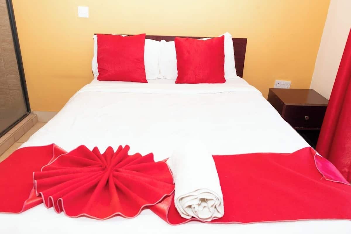 A neatly made bed with white and red bedding, a wooden headboard, and a small bedside table with a red curtain.
