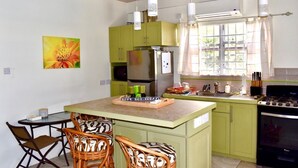 Una cocina con armarios verdes, un refrigerador de acero inoxidable, una estufa y un comedor con sillas de mimbre.