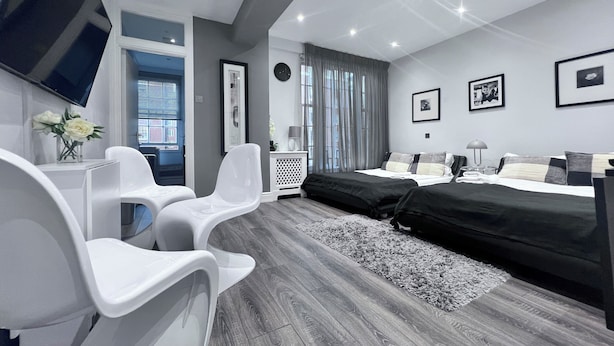 Ein modernes Schlafzimmer mit einem Bett, zwei weißen Stühlen, einem Schreibtisch und einem Fernseher.