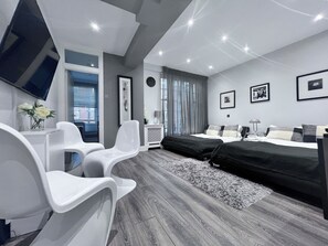 Une chambre moderne avec un lit, deux chaises blanches, un bureau et un téléviseur.