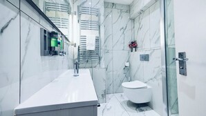 Ein modernes Badezimmer mit Marmor-Spritzschutz, einer Glasdusche und einer weißen Toilette.
