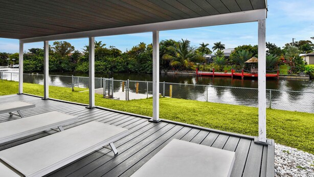 Eine überdachte Terrasse mit Bänken, die auf einen ruhigen Fluss mit üppiger Ufervegetation und einer roten Brücke in der Ferne blickt.