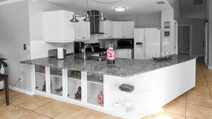 Eine moderne Küche mit weißen Schränken, Granit Arbeitsplatten und einer eingebauten Kochinsel mit Spüle und Stauraum.