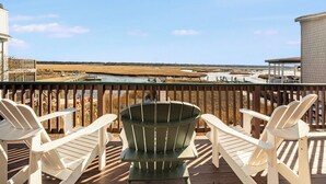 Une terrasse dotée de chaises Adirondack blanches et d’une chaise Adirondack verte, offrant une vue sur une plage et des marais.