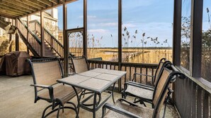 Un espace extérieur abrité avec une table et des chaises, un barbecue couvert et une vue sur un champ.