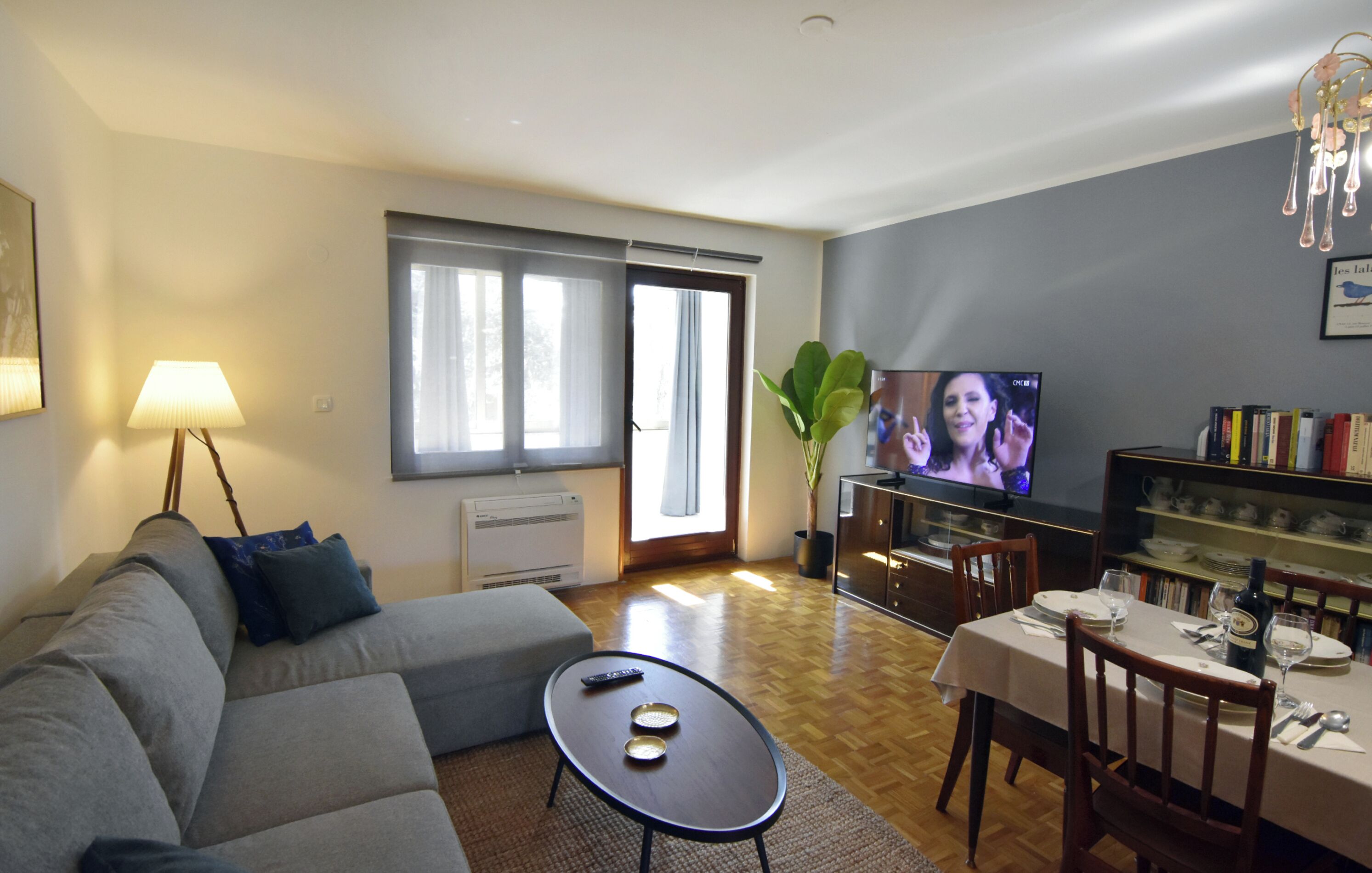 A living room with a sofa, a coffee table, a TV, and a dining area with a table set for two.