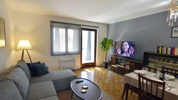A living room with a sofa, a coffee table, a TV, and a dining area with a table set for two.