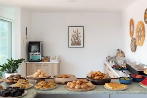 A breakfast buffet with various pastries, a coffee machine, and a decorative wall piece.