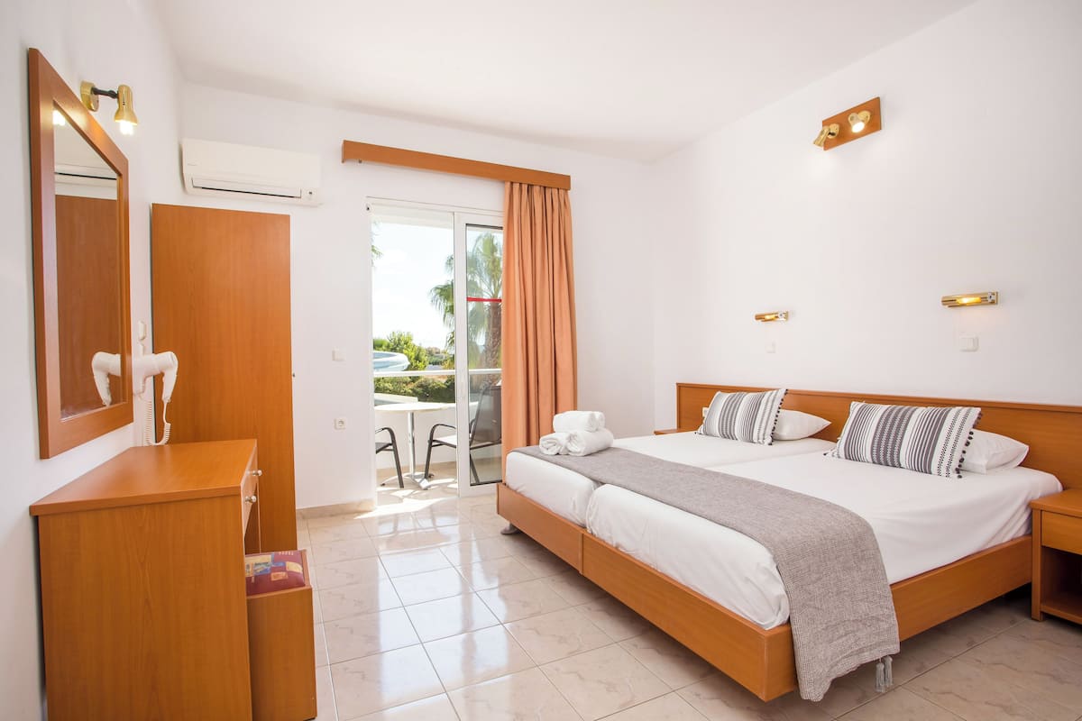 A hotel room with a bed, a desk, a chair, and a sliding glass door to a balcony.