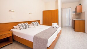 Habitació d'hotel amb un llit de fusta, una tauleta de nit, un bany amb mirall i un lavabo, i un armari.