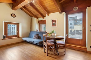 Um quarto com teto de madeira, um sofá, uma mesa de jantar com cadeiras, uma janela com persianas e uma porta com janela.