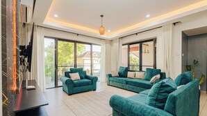 Ein geräumiges Wohnzimmer mit türkisfarbenen Sofas, einem Flachbildfernseher und einer großen Schiebetür, die auf einen Balkon führt.
