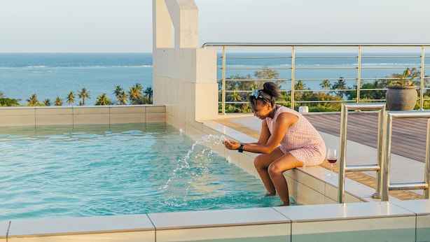 Eine Person sitzt am Pool mit Blick auf den Ozean.