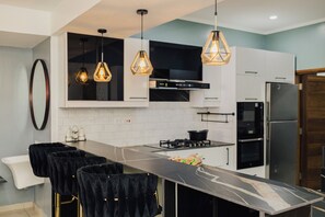 A modern kitchen with a marble countertop, black chairs, and pendant lighting.