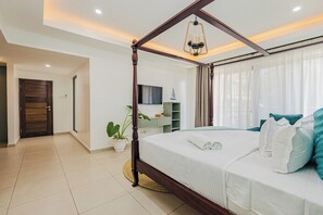 A modern bedroom with a four-poster bed, a large window with sheer curtains, and a small potted plant.