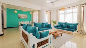 Ein modernes Wohnzimmer mit türkisfarbenen Sofas, einem weißen Sofa, einem Holztisch und einem Bett mit weißem Rahmen.
