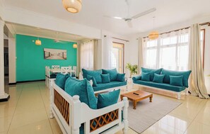 Un salon moderne avec des canapés de couleur turquoise, un canapé blanc, une table basse en bois et un lit avec un cadre blanc.