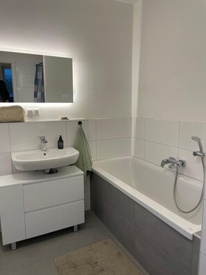 A modern bathroom with a white sink, mirror, and bathtub. - Feel-Good Oasis Near the Trade Fair (Sehnde)