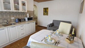 Una cocina moderna con armarios blancos, microondas y un lavabo. Hay una zona de comedor con una mesa preparada para dos personas, con mantel blanco y una botella de champán.