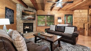 Ein gemütliches Blockhaus-Interieur mit Kamin aus Stein, Ledersofa und Deckenventilator.