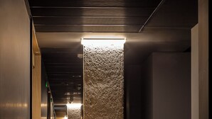 A hallway with a textured column, carpeted floor, and a series of doors on the left. - Hotel Iriguibel Arrosadía (Pamplona)