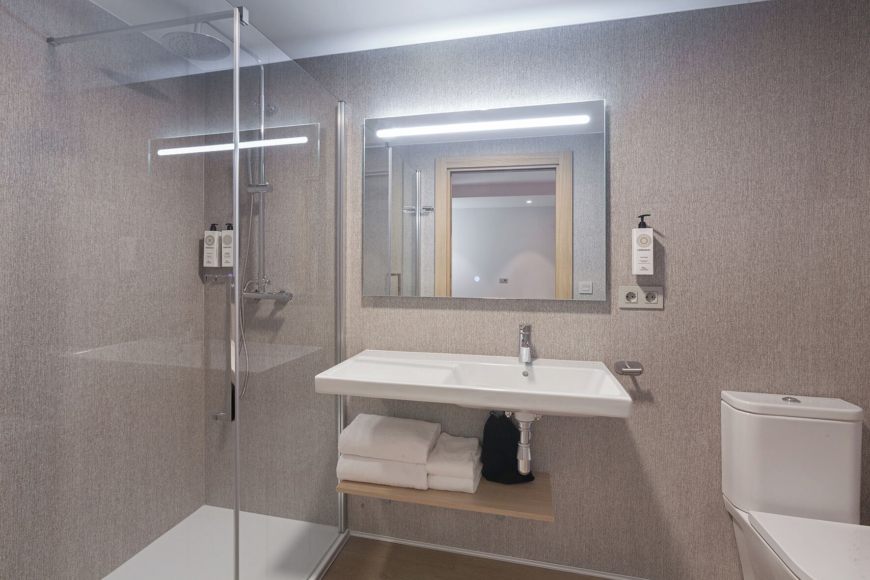 Une salle de bain moderne avec une douche à parois de verre, un lavabo blanc avec un miroir au-dessus et des toilettes.