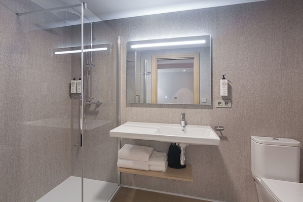 A modern bathroom with a glass-enclosed shower, a white sink with a mirror above it, and a toilet. - Hotel Iriguibel Arrosadía (Pamplona)