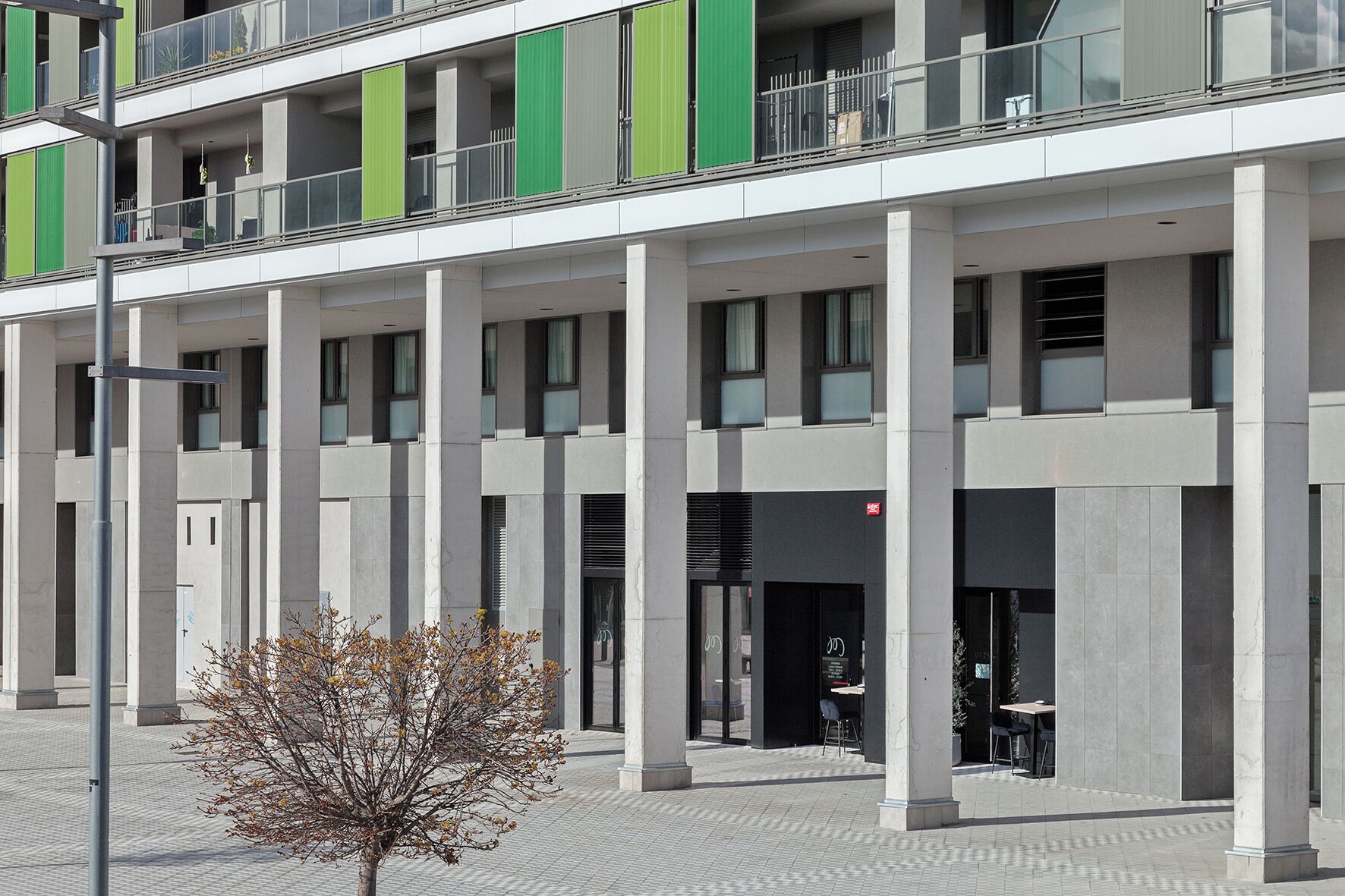 Ein mehrstöckiges Gebäude mit moderner Architektur, das durch eine Reihe von Säulen und Balkonen gekennzeichnet ist.