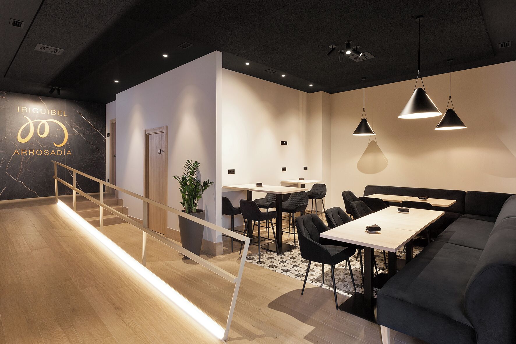 Un interior moderno con una escalera, un comedor con mesas y sillas, y un sofá.