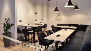 A modern meeting room with a long table, black chairs, a dark sofa, and pendant lighting.