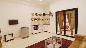 A modern living room with a sofa, a coffee table, and a kitchen area with a refrigerator, oven, and tiled backsplash. - NOOR SEEN HOUSE  (Luxor)