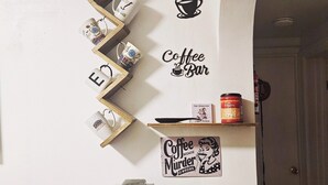 A coffee-themed wall with shelves holding mugs, a coffee machine, and a sign saying 'Coffee Bar.'