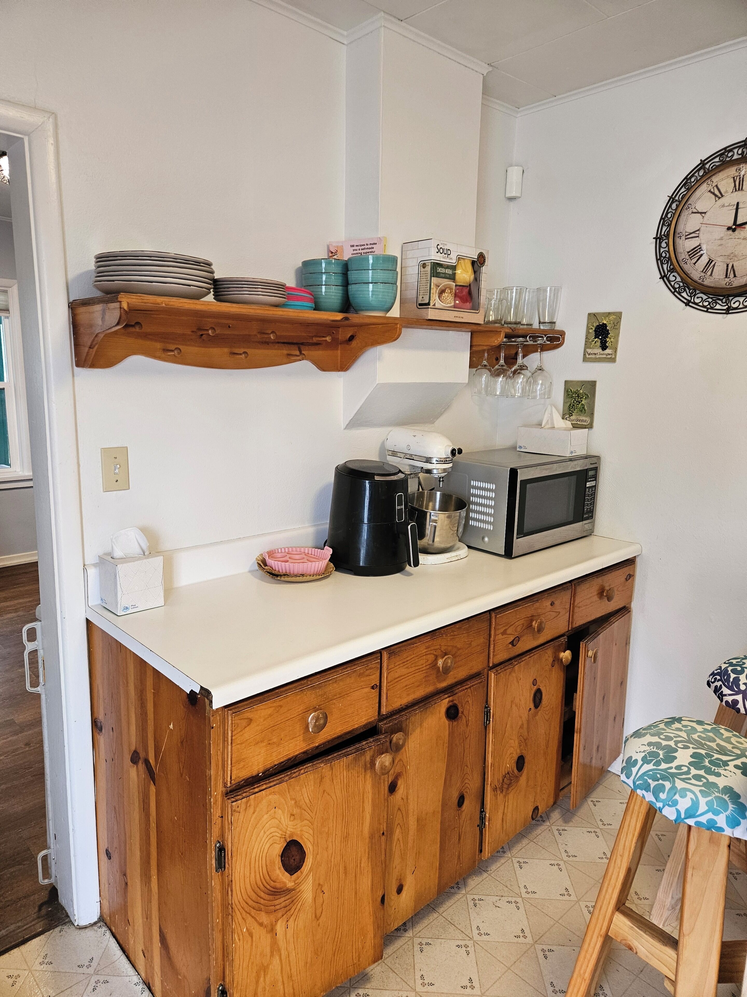 A kitchen with wooden cabinets, a microwave, a coffee maker, and a clock on the wall.