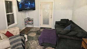 A living room with a television mounted on the wall, a couch, a chair, and a patterned rug.
