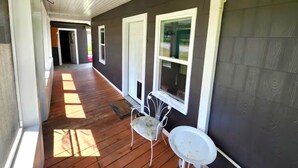 A covered porch with wooden flooring, white railings, and a white table.