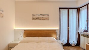 Un dormitorio con cama, mesitas de noche, cortinas en la ventana y una obra de arte colgada en la pared.