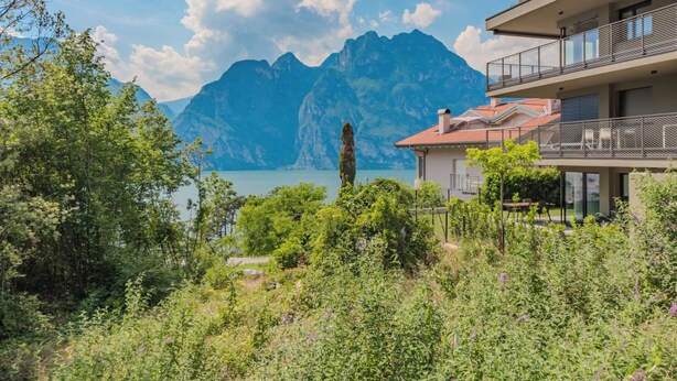 Un edificio moderno con balcón que da a un paisaje montañoso y un lago.