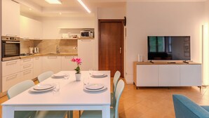 Una cocina moderna con electrodomésticos, un comedor con mesa dispuesta para cuatro personas y una sala de estar con televisor.