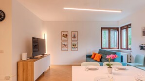 Una sala de estar moderna con comedor, televisión, obras de arte en las paredes y ventanas amplias.
