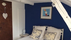 Ein Schlafzimmer mit einem Bett, zwei Kissen, einem Nachttisch, einem gerahmten Bild und einer herzförmigen Dekoration an der Wand.