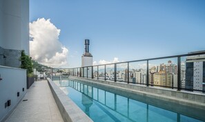 Une piscine sur le toit offrant une vue sur la ville, une rambarde en verre et une haute cheminée.