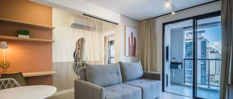 A modern living room with a grey sofa, a white table, and a large window with a city view.