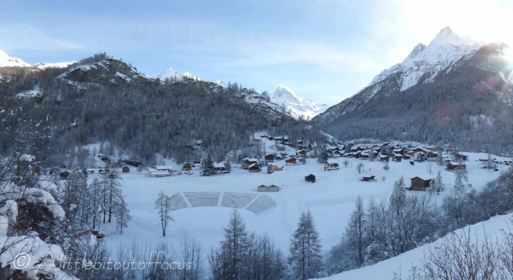 Un village de montagne enneigé, avec ses maisons traditionnelles en bois, une piste de ski et une vue dégagée sur les sommets environnants.