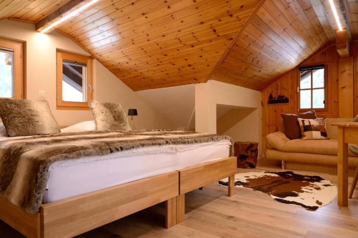 A cozy bedroom with a wooden ceiling, a bed with a fur throw, a cowhide rug, and a window with a view.