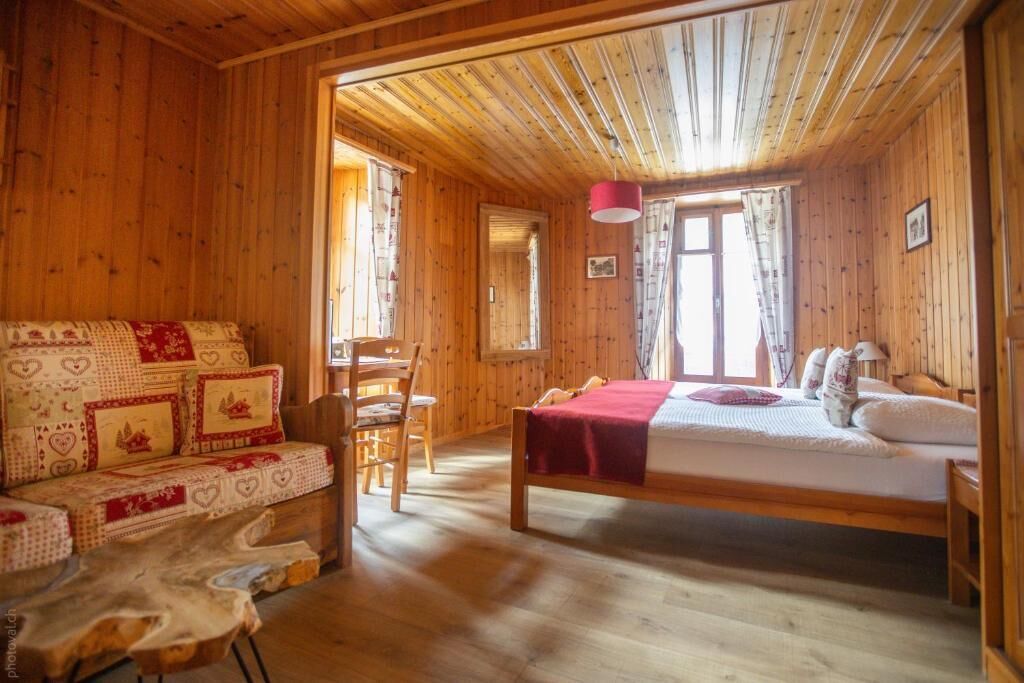 A wooden cabin room with a bed, a sofa, and a dining table.
