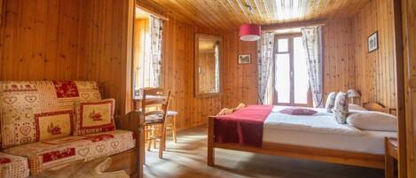 A wooden cabin room with a bed, a sofa, and a dining table.