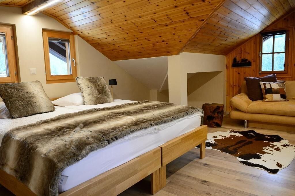 Una habitación acogedora con techo de madera, cama con manta de piel, sofá de cuero y alfombra de cuero de vaca.