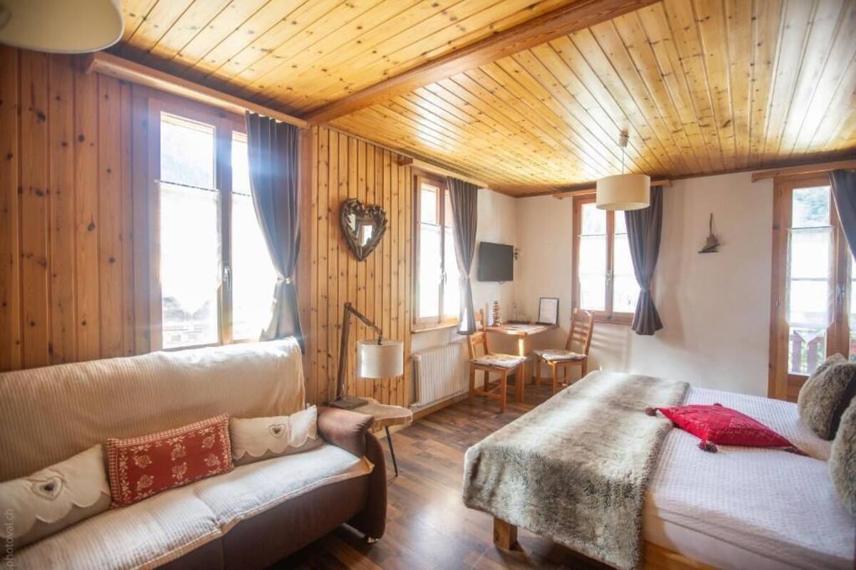 A cozy room with wooden walls and ceiling, a sofa, a bed, a desk, and a television.