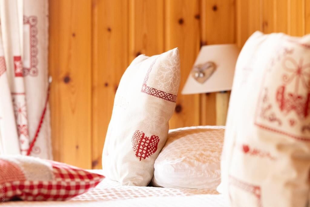 Un lit avec une literie blanche et des coussins décoratifs, dont un avec un motif en forme de cœur, dans une pièce aux murs lambrissés.